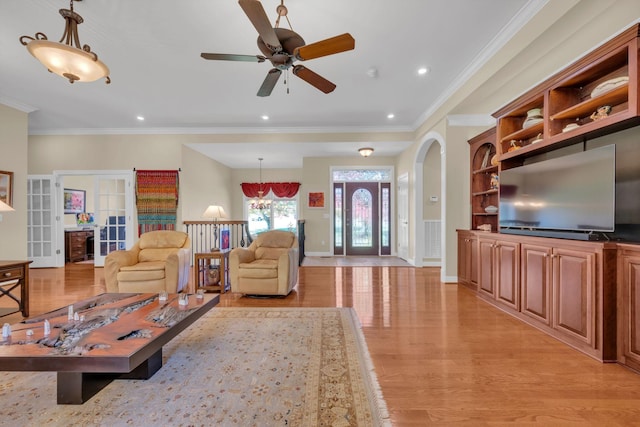 living room with crown molding, recessed lighting, light wood-style flooring, ceiling fan with notable chandelier, and arched walkways