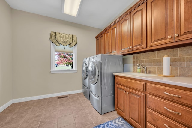 washroom with visible vents, baseboards, washer and dryer, cabinet space, and a sink