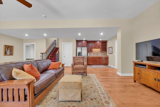 living area with light wood-type flooring, recessed lighting, baseboards, ceiling fan, and stairs