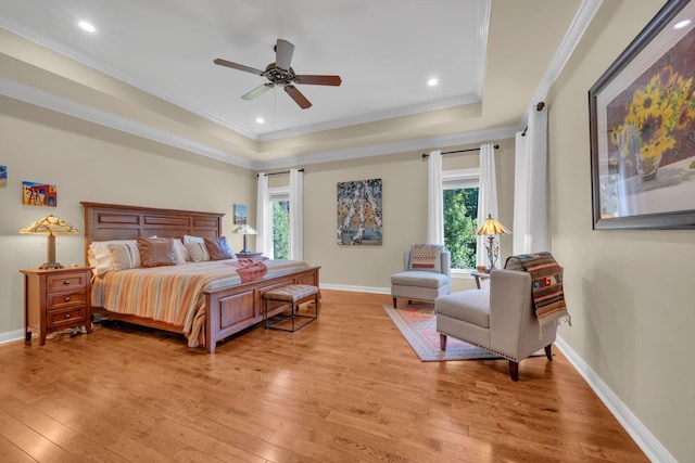 bedroom with a raised ceiling, multiple windows, light wood-type flooring, and ornamental molding