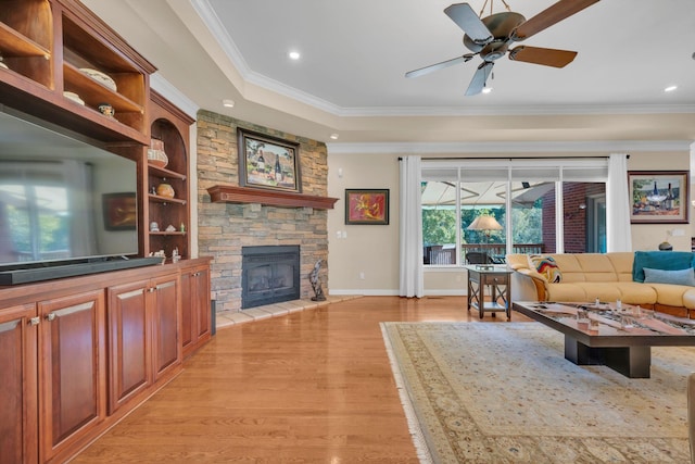 living area with light wood finished floors, baseboards, ceiling fan, ornamental molding, and a stone fireplace