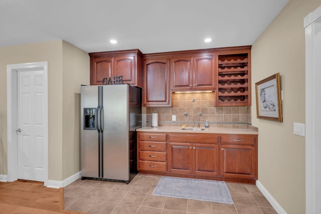 kitchen featuring tasteful backsplash, light countertops, stainless steel refrigerator with ice dispenser, and a sink