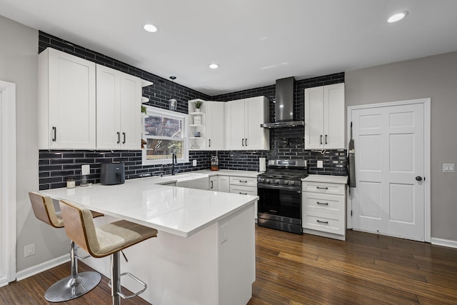 kitchen with a peninsula, open shelves, stainless steel range with gas stovetop, a sink, and wall chimney range hood