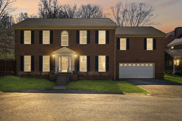 colonial-style house featuring a front yard, fence, driveway, a garage, and brick siding