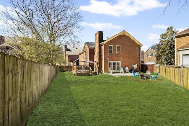 back of property with a wooden deck, a lawn, a fenced backyard, and a chimney