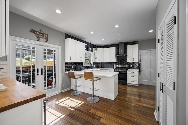 kitchen with a sink, a kitchen breakfast bar, dark wood finished floors, wall chimney exhaust hood, and black range with gas stovetop