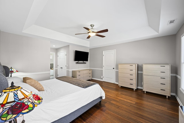 bedroom featuring visible vents, a tray ceiling, dark wood finished floors, baseboards, and ceiling fan