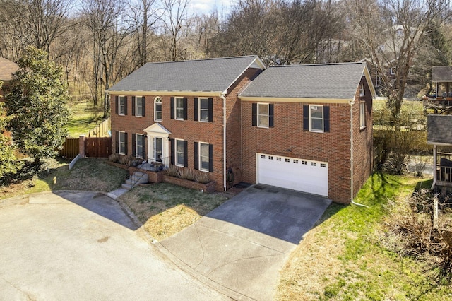 colonial-style house featuring fence, roof with shingles, an attached garage, concrete driveway, and brick siding