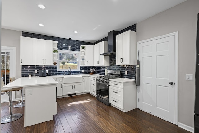 kitchen with a sink, open shelves, a peninsula, wall chimney range hood, and stainless steel range with gas stovetop