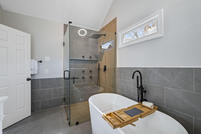 bathroom with tile patterned flooring, a shower stall, vaulted ceiling, a soaking tub, and tile walls