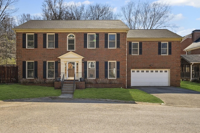 colonial-style house with brick siding, driveway, a front lawn, and fence