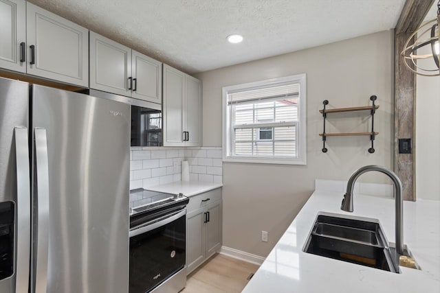 kitchen featuring a sink, decorative backsplash, light countertops, stainless steel appliances, and light wood-style floors