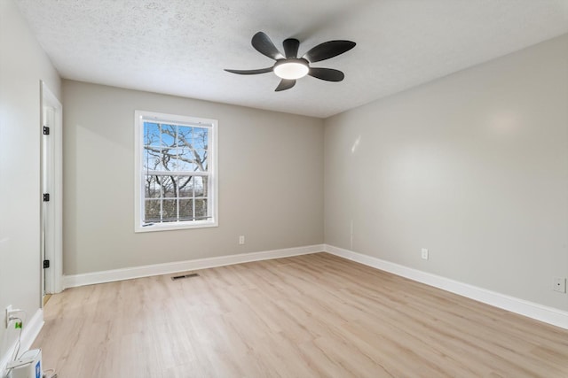 spare room with baseboards, visible vents, light wood finished floors, ceiling fan, and a textured ceiling