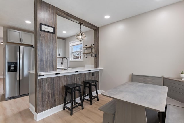 kitchen with a breakfast bar area, a sink, light countertops, stainless steel refrigerator with ice dispenser, and light wood-type flooring