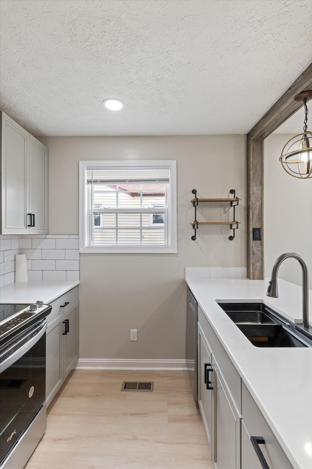 kitchen with visible vents, backsplash, gray cabinets, appliances with stainless steel finishes, and a sink