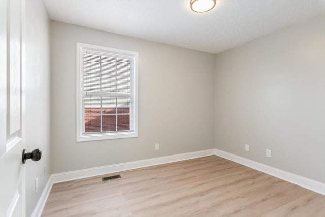 empty room with visible vents, a textured ceiling, light wood-style floors, and baseboards