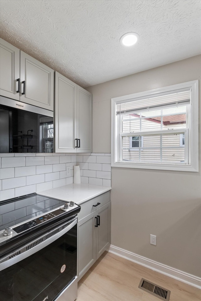 kitchen featuring visible vents, light wood-style flooring, gray cabinets, electric range oven, and tasteful backsplash