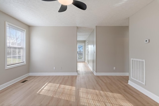 spare room featuring visible vents, a ceiling fan, a textured ceiling, light wood finished floors, and baseboards