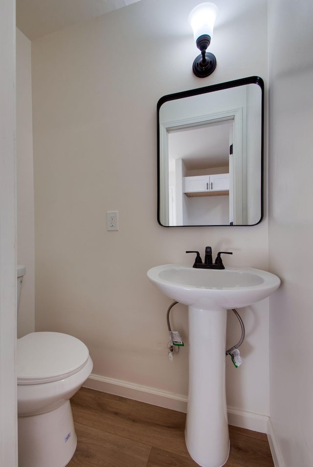 half bath with toilet, wood finished floors, and baseboards