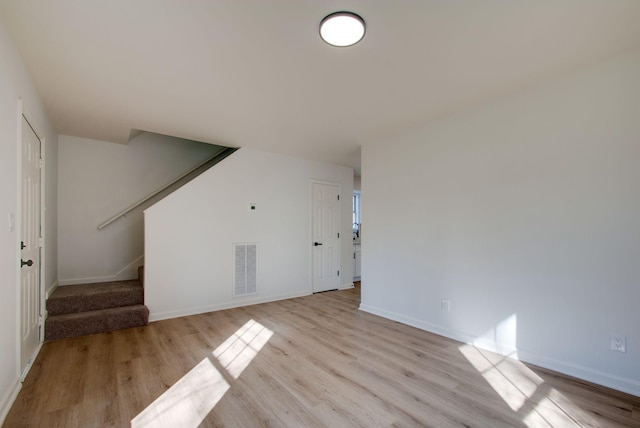 unfurnished living room with light wood finished floors, stairway, baseboards, and visible vents