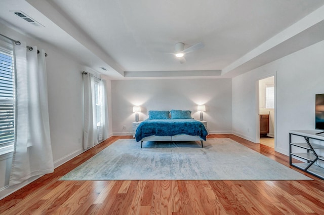 bedroom with visible vents, a raised ceiling, baseboards, and wood finished floors