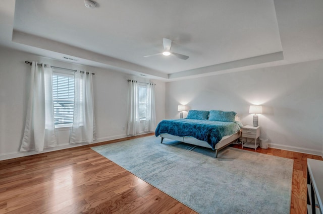 bedroom with multiple windows, a raised ceiling, and wood finished floors