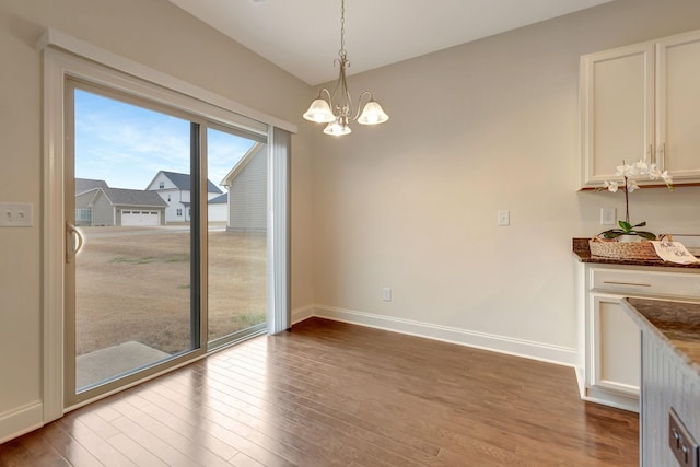 unfurnished dining area with baseboards, an inviting chandelier, and wood finished floors