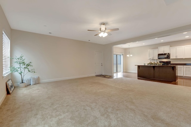 unfurnished living room with light carpet, recessed lighting, ceiling fan with notable chandelier, and baseboards