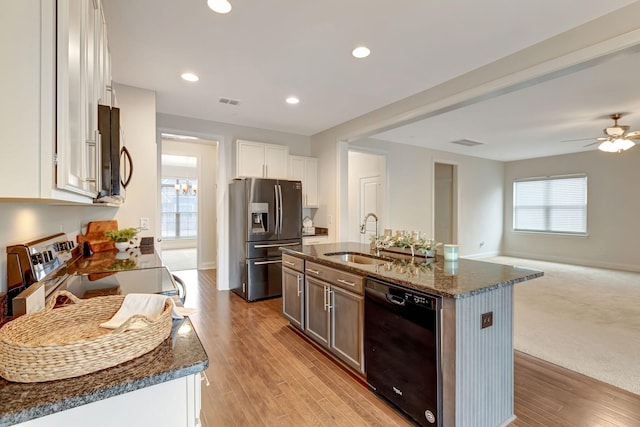 kitchen featuring light wood finished floors, dark stone counters, a sink, stainless steel appliances, and open floor plan