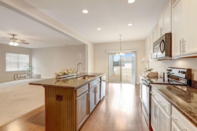 kitchen featuring a breakfast bar area, wood finished floors, dark stone counters, a sink, and stainless steel appliances