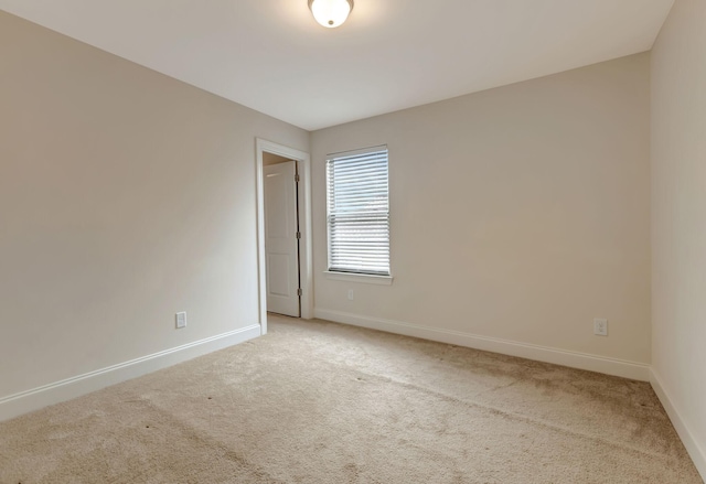 spare room featuring light colored carpet and baseboards