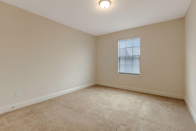 spare room featuring light colored carpet and baseboards