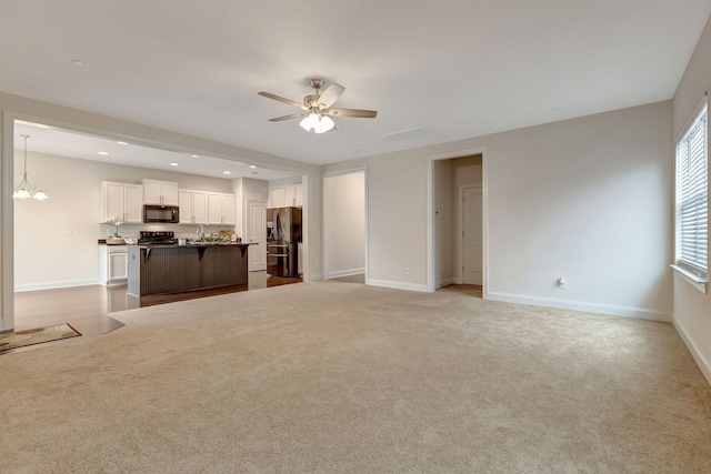 unfurnished living room with ceiling fan with notable chandelier, a sink, recessed lighting, baseboards, and light colored carpet