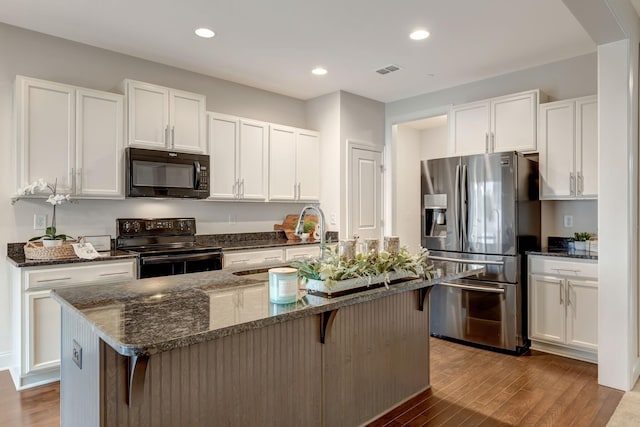 kitchen featuring black appliances, dark stone counters, wood finished floors, white cabinetry, and a sink