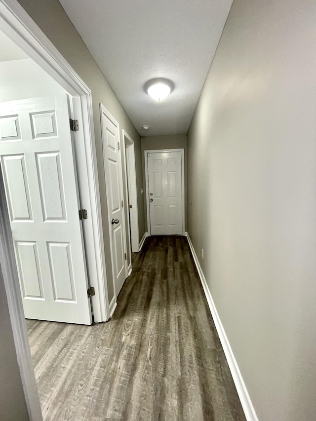 hallway featuring baseboards, a textured ceiling, and wood finished floors