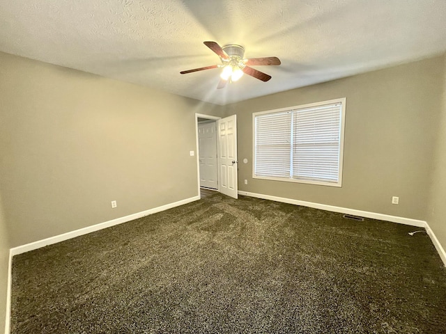 unfurnished room with a textured ceiling, baseboards, dark colored carpet, and ceiling fan