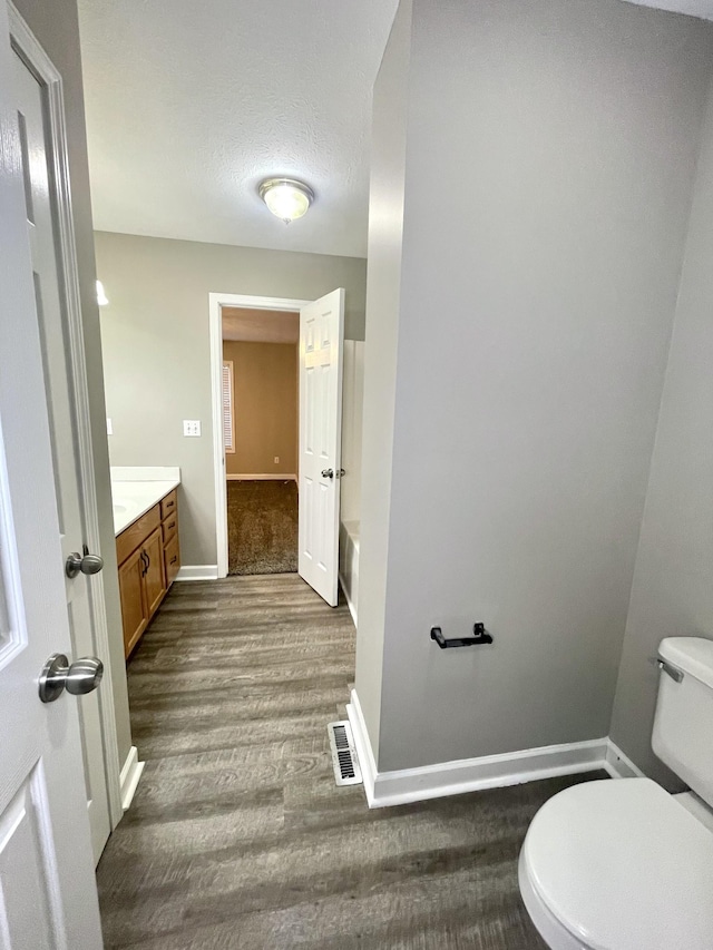 bathroom with baseboards, toilet, wood finished floors, a bath, and vanity