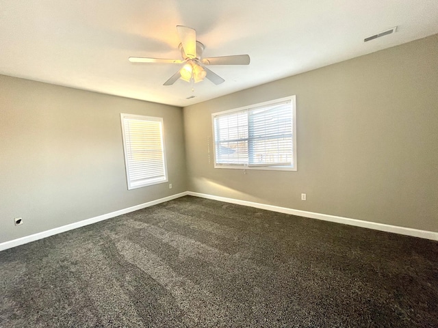 unfurnished room featuring visible vents, a ceiling fan, baseboards, and dark colored carpet