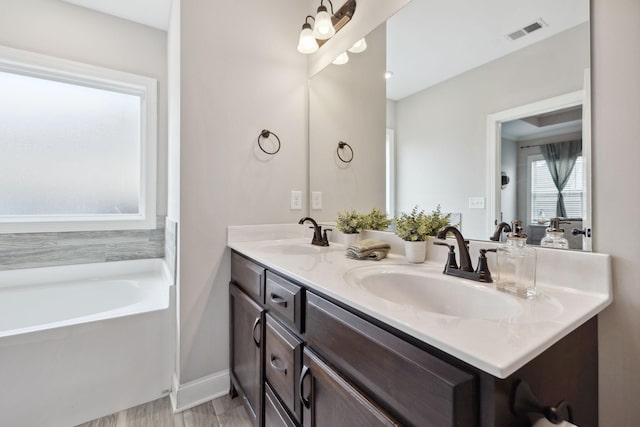 full bathroom featuring double vanity, a tub to relax in, visible vents, and a sink