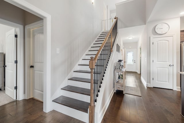 stairs featuring baseboards, a towering ceiling, and hardwood / wood-style flooring