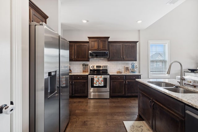 kitchen with a sink, backsplash, dark brown cabinetry, appliances with stainless steel finishes, and dark wood-style flooring