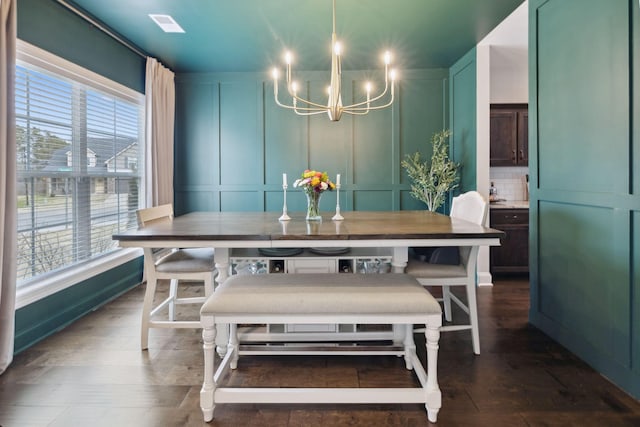 dining area featuring dark wood finished floors, a decorative wall, and a chandelier