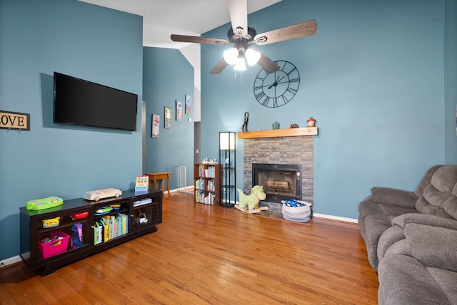 living room with baseboards, ceiling fan, vaulted ceiling, a stone fireplace, and wood finished floors