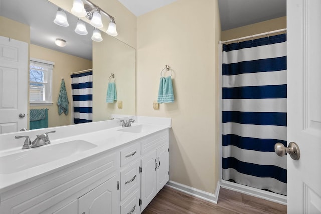 full bath with double vanity, wood finished floors, baseboards, and a sink