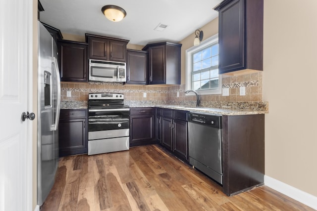 kitchen with wood finished floors, a sink, stainless steel appliances, dark brown cabinetry, and backsplash