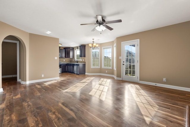 unfurnished living room featuring baseboards, ceiling fan with notable chandelier, dark wood-style flooring, and arched walkways