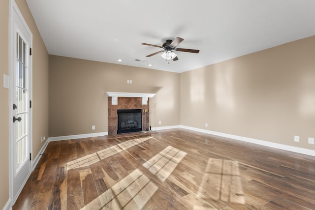 unfurnished living room with wood finished floors, a ceiling fan, baseboards, and a tile fireplace