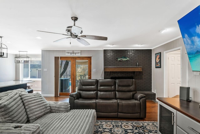 living room with ceiling fan with notable chandelier, a brick fireplace, crown molding, and dark wood-style flooring