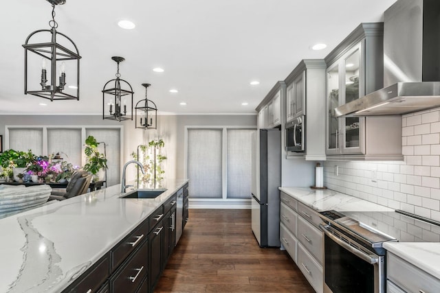 kitchen featuring a sink, wall chimney range hood, a chandelier, appliances with stainless steel finishes, and dark wood-style flooring