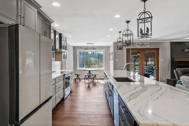 kitchen with light stone countertops, decorative light fixtures, appliances with stainless steel finishes, dark wood-style floors, and a sink